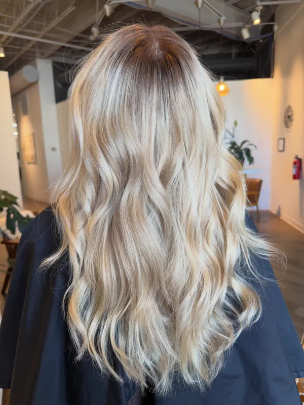Long bright blonde hair in soft waves with a blended shadow root